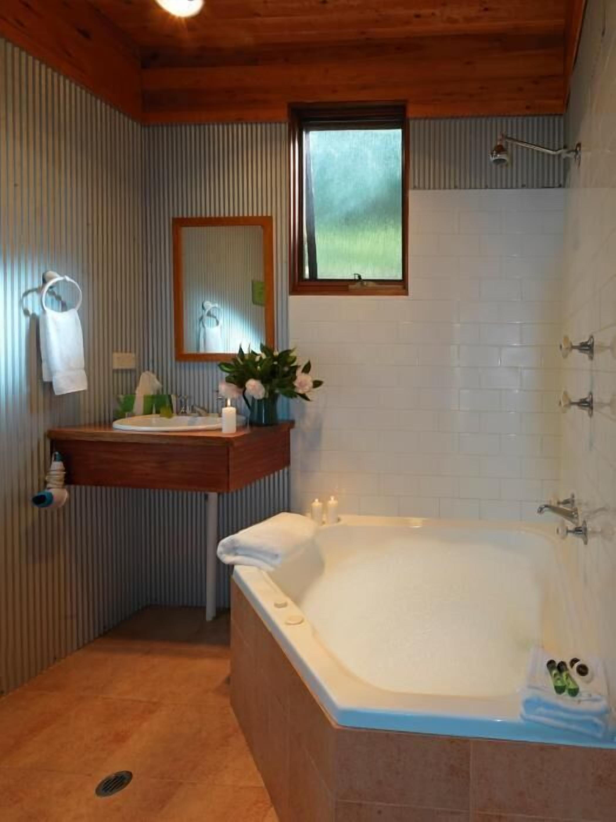 A bathroom with a wooden ceiling, a large bathtub, a sink with a mirror above it, and a window.