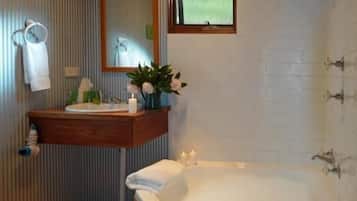 A bathroom with a wooden ceiling, a large bathtub, a sink with a mirror above it, and a window.