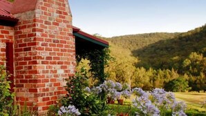 Un bâtiment en briques surmonté d’un toit rouge, entouré d’une végétation luxuriante et de fleurs violettes.