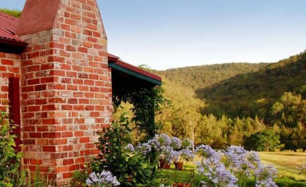 A brick building with a red roof, surrounded by lush greenery and purple flowers. - Cedar Creek Cottages (Sweetmans Creek)
