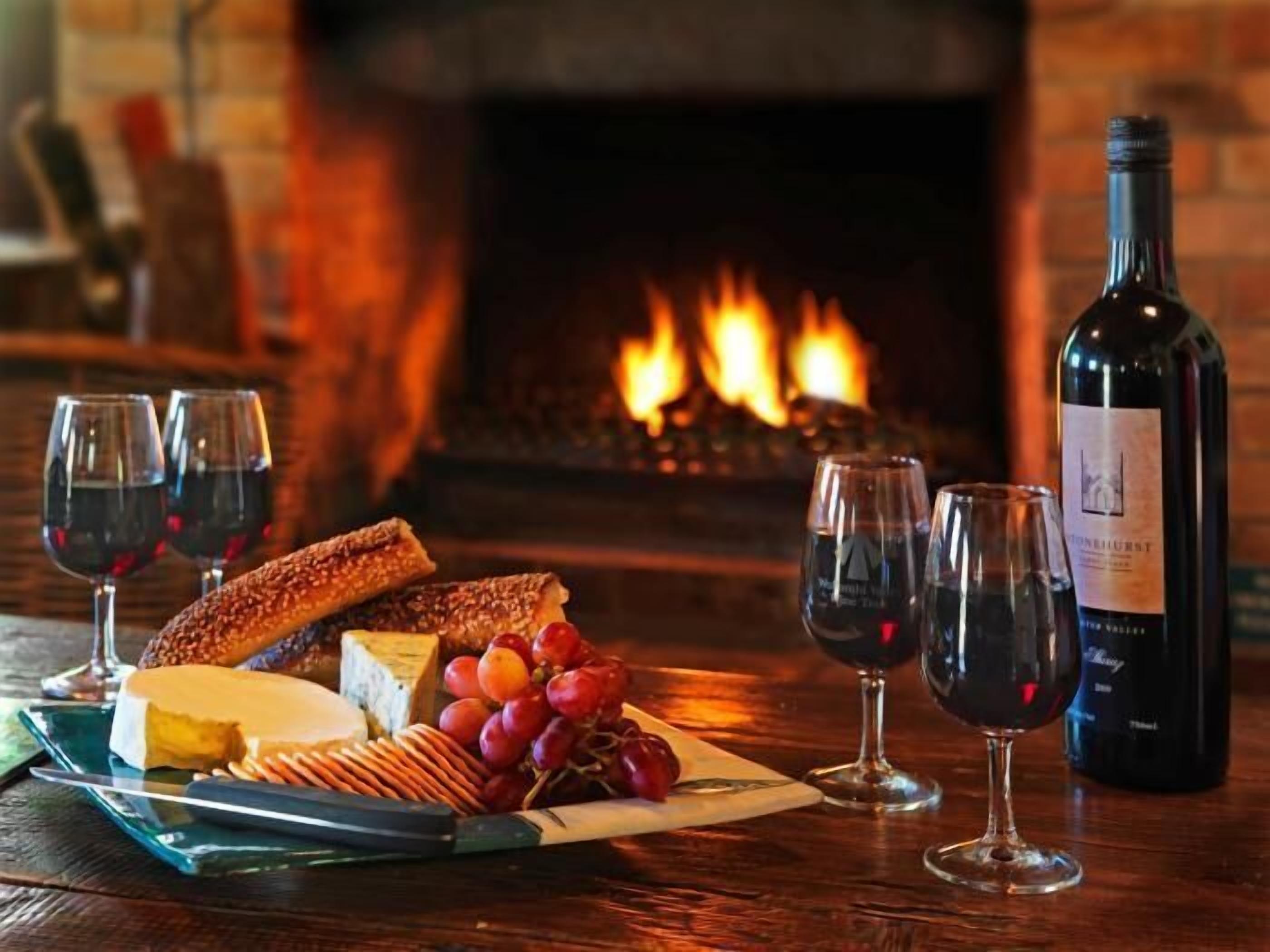 Una mesa con queso, uvas, galletas y copas de vino frente a una chimenea.