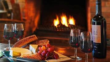 Una mesa con queso, uvas, galletas y copas de vino frente a una chimenea.