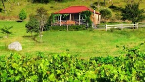 Un bâtiment à toit rouge, entouré de verdure, avec une clôture blanche et un grand rocher à proximité.