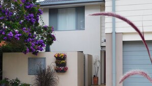 A modern house with a beige exterior, a grey garage door, and a small garden area with potted plants and a flower box on the wall. - Beachport Bed and Breakfast (Port Macquarie)