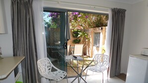 A small, well-lit room with a glass door leading to an outdoor area. Inside, there is a table with two white chairs, a small white fridge, and a green bucket. - Beachport Bed and Breakfast (Port Macquarie)