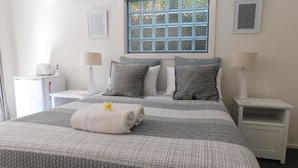 A neatly arranged hotel room with a bed, two bedside tables, a window, and a small desk with a lamp. - Beachport Bed and Breakfast (Port Macquarie)