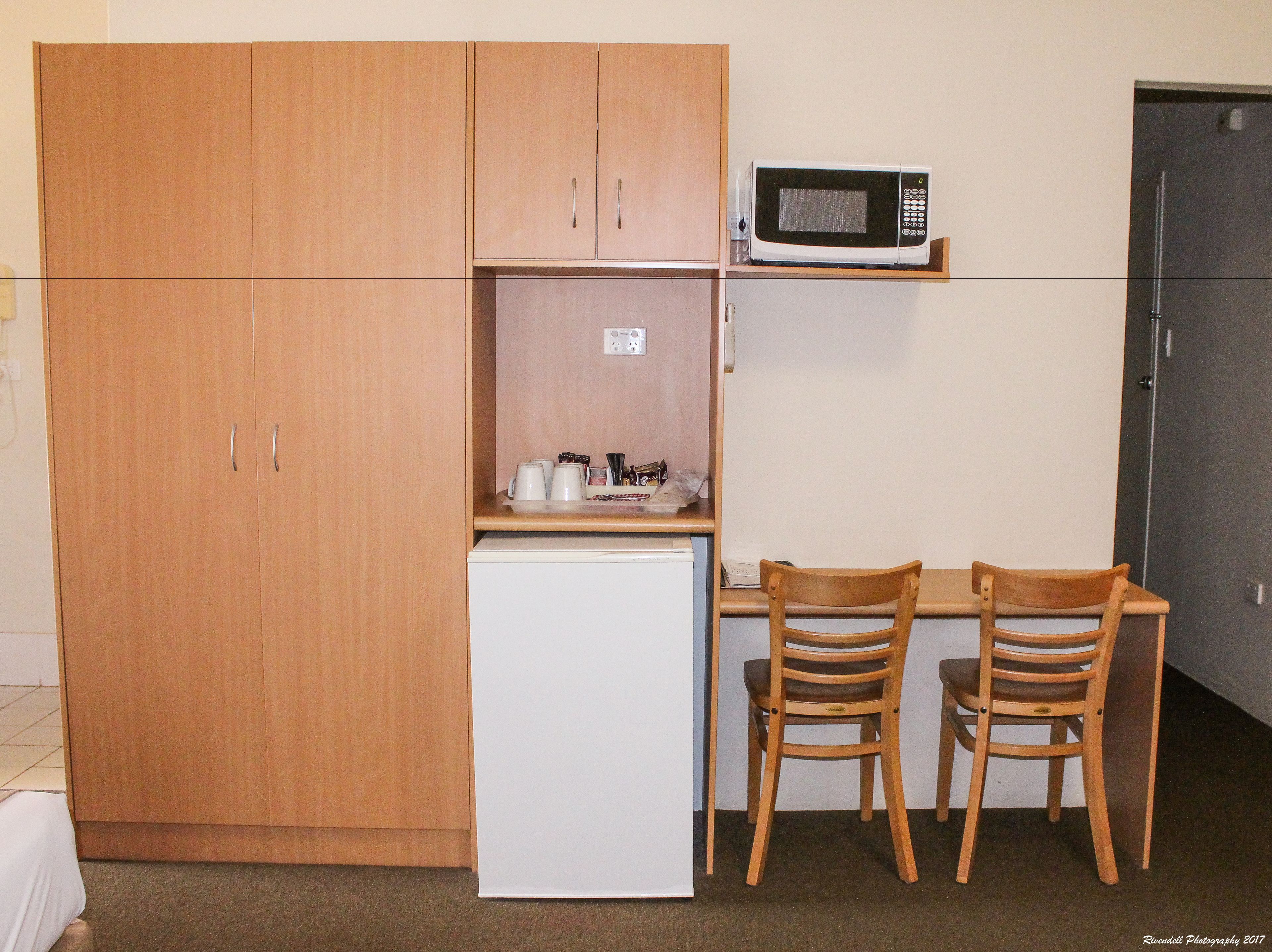 A compact kitchenette with a microwave, a small refrigerator, and two wooden chairs.