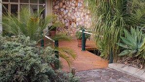 A stone wall, a wooden deck, and various plants. - Motel Riverina (Leeton)