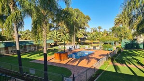 A well-maintained outdoor area with a swimming pool, palm trees, and a brick pathway. - Motel Riverina (Leeton)