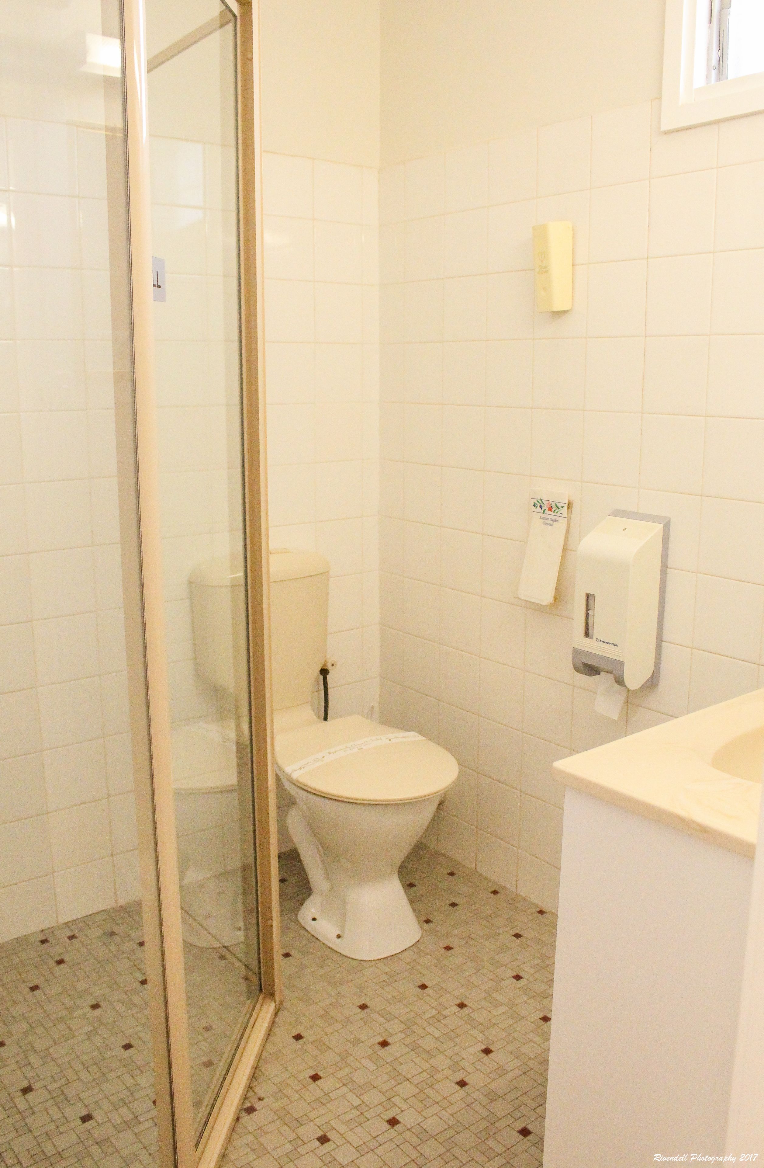 A bathroom with a toilet, a glass shower enclosure, and a hand dryer.