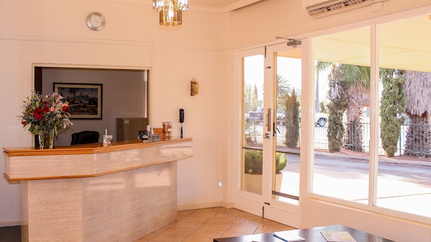 A reception area with a desk, chairs, a clock, and a large window with a view of the street. - Motel Riverina (Leeton)