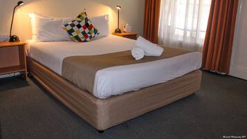 A neatly made bed with a checkered pillow, a rolled towel, and two bedside lamps.