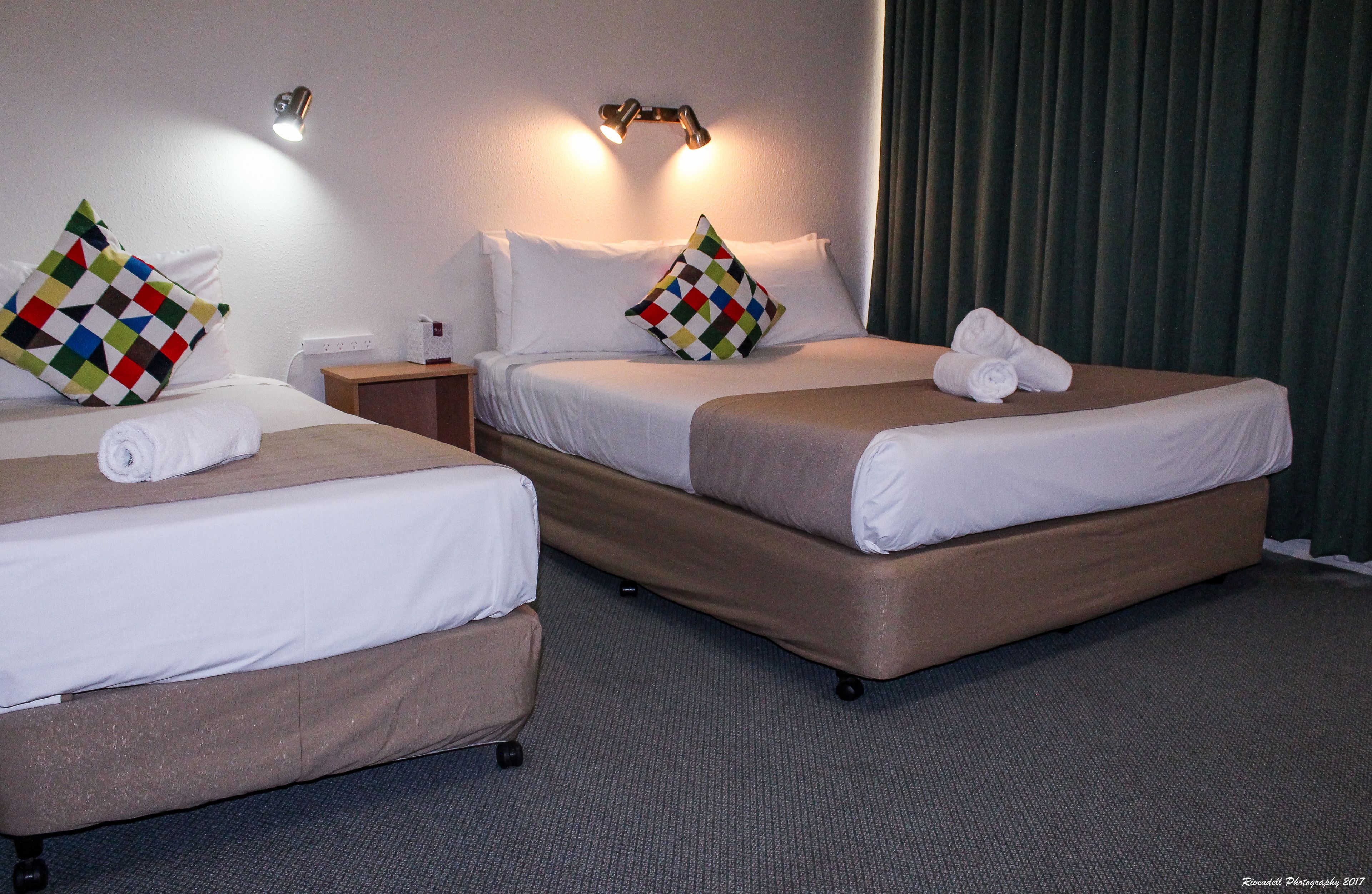 A hotel room with two beds, each with a pillow and a rolled towel.