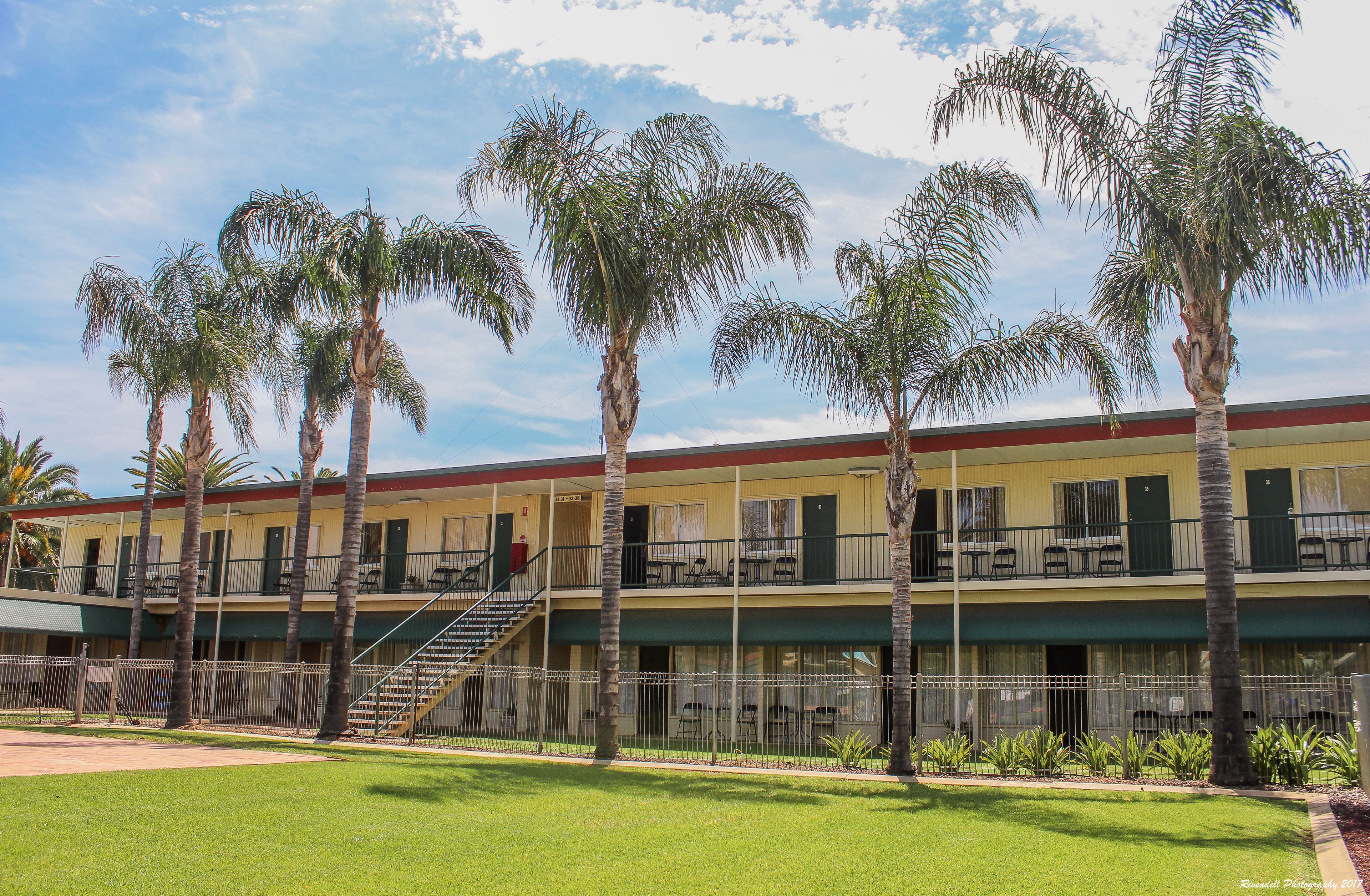 Un motel de dos pisos con techo rojo, varios balcones y palmeras en el patio.