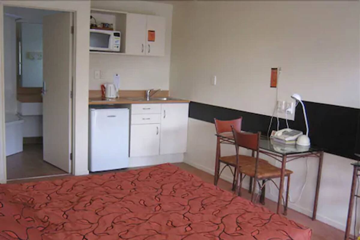 A room with a bed, a desk, a chair, a microwave, a sink, and cabinets.