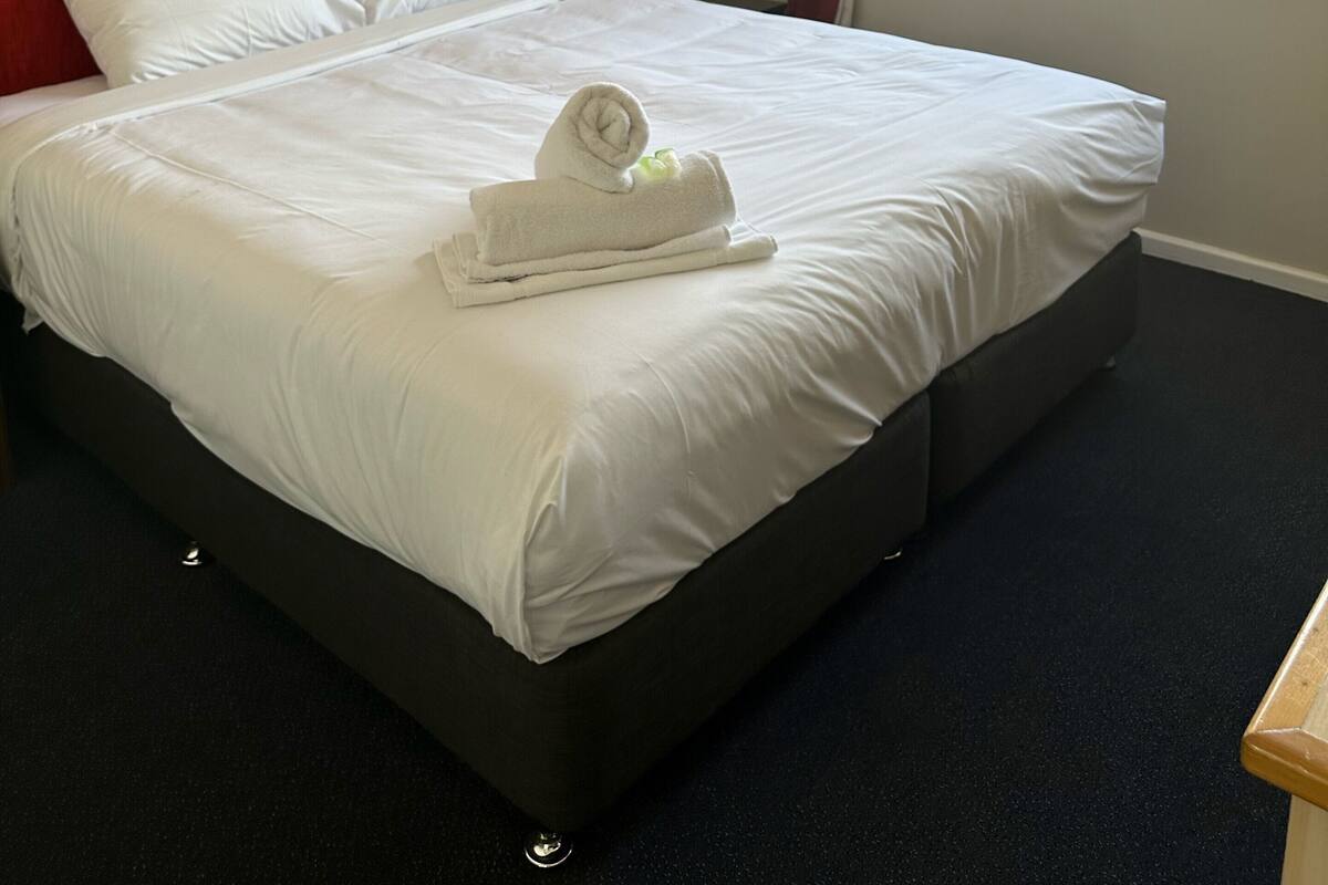 A hotel room with a large bed, a red headboard, a window with curtains, and an air conditioning unit.