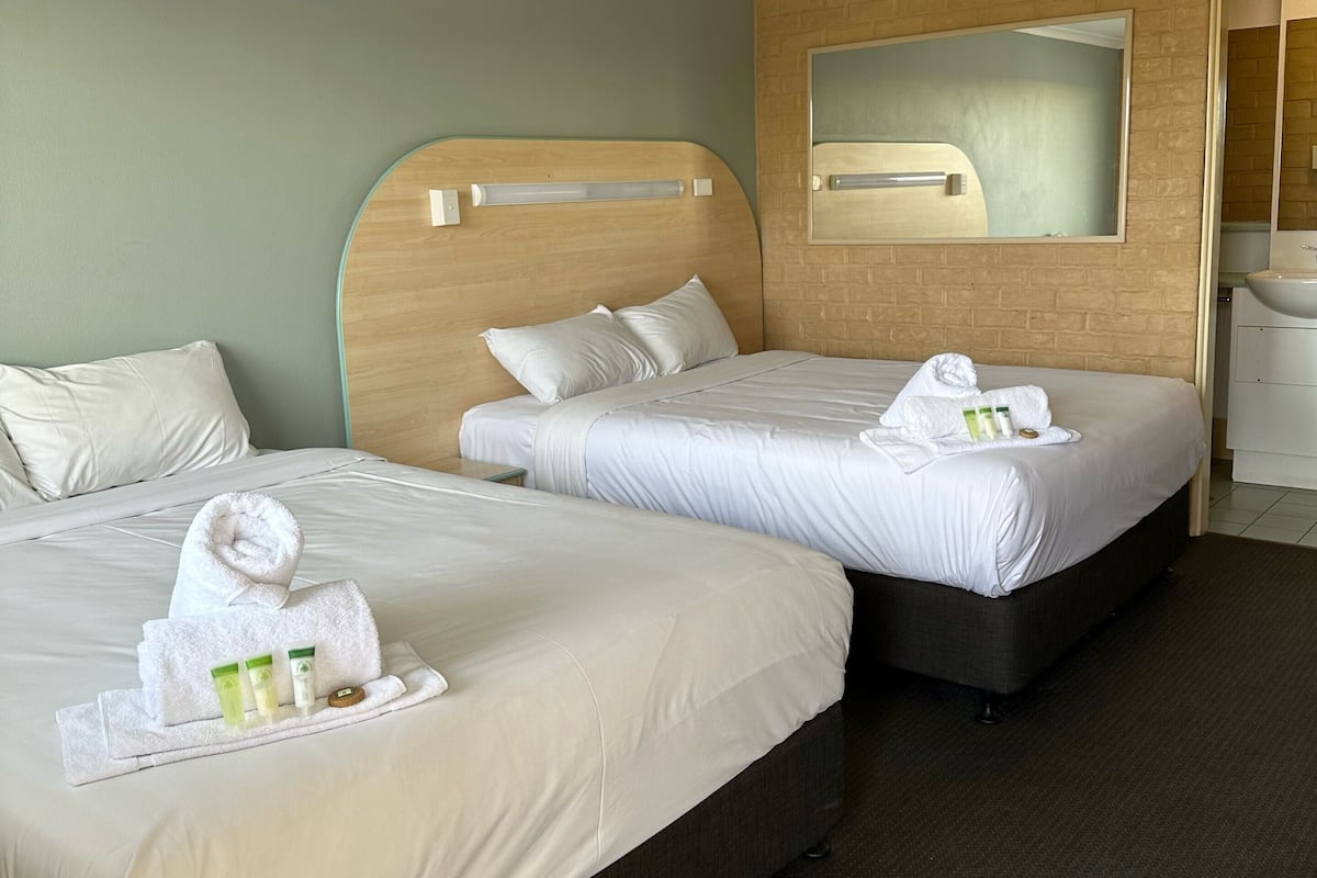 A hotel room with two beds, a wooden headboard, a large mirror, and a bathroom with a sink and mirror.