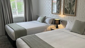 A hotel room with two beds, a hanging light fixture, a window with curtains, and framed botanical artwork on the wall. - Shamrock Hotel Motel (Toowoomba)