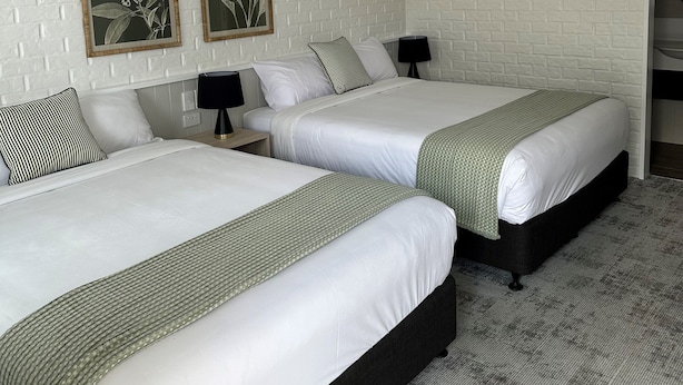 A hotel room with two beds, white brick-patterned walls, and two framed botanical prints. - Shamrock Hotel Motel (Toowoomba)
