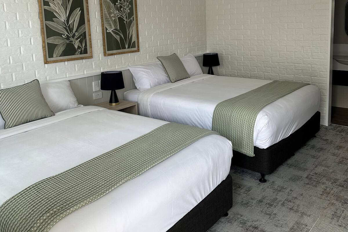 A hotel room with two beds, white brick-patterned walls, and two framed botanical prints.