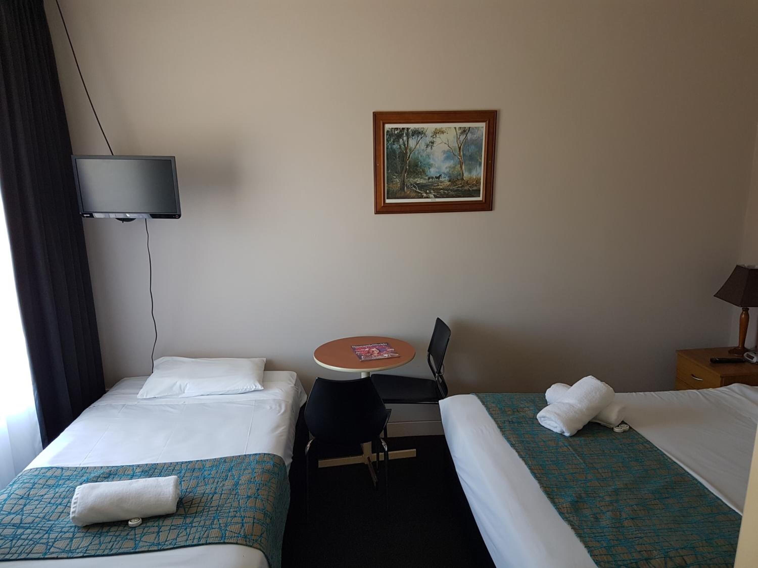 Une chambre d’hôtel avec deux lits, un bureau avec une chaise, une télévision et un tableau au mur.