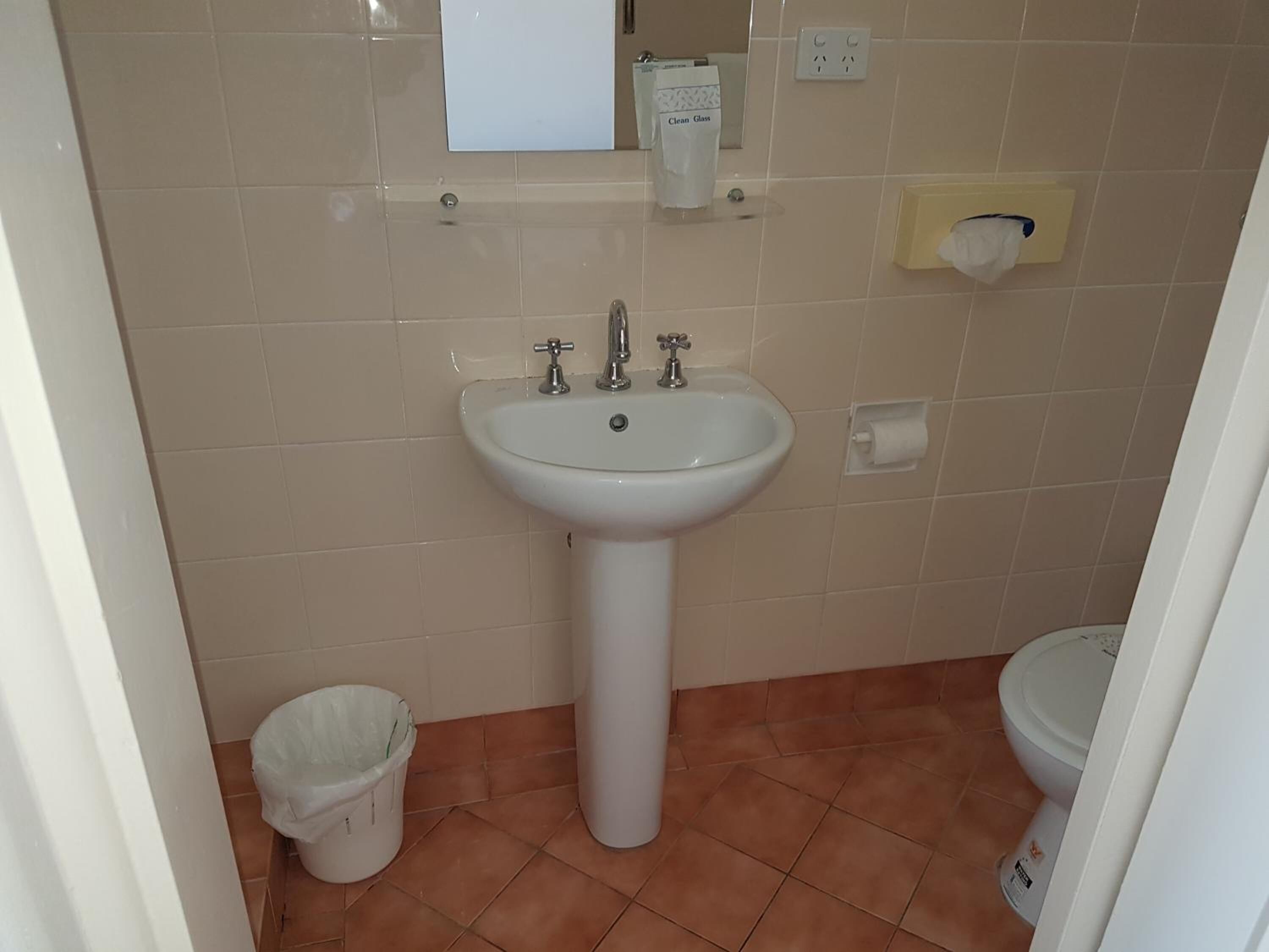 Un baño con lavamanos pedestal blanco, inodoro y un cubo de basura.