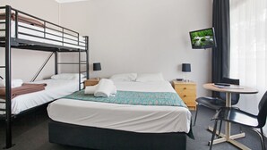A hotel room with a bunk bed, a single bed, a TV, a desk with a chair, and a window with curtains.