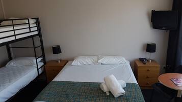 Een hotelkamer met een stapelbed, een enkel bed, twee nachtkastjes met lampen, een televisie aan de muur en een klein rond tafeltje met een tijdschrift.