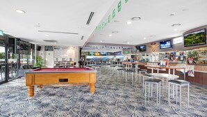 A pool table in a hotel lobby with a bar area and seating.