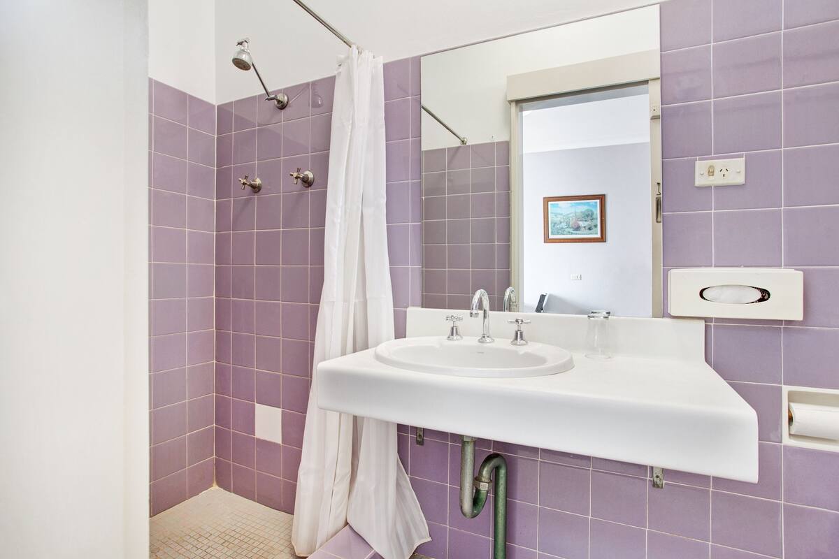 A bathroom with purple tiles, a white sink, and a shower with a curtain.