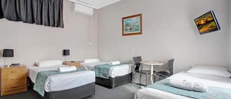 Une chambre d’hôtel avec deux lits, un bureau et une chaise. Il y a un tableau au mur et un appareil de climatisation.