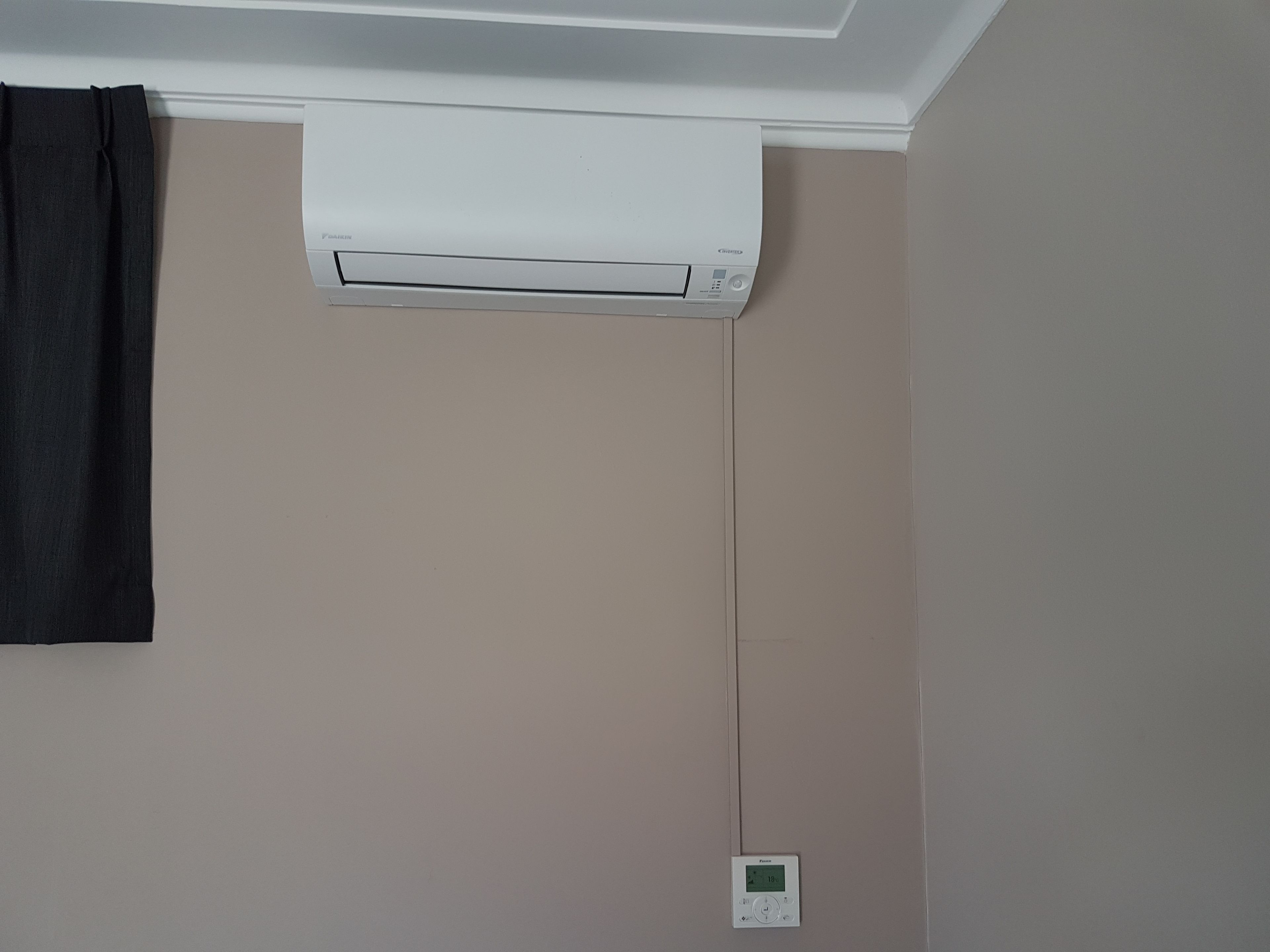 A room with a white ceiling-mounted air conditioner and a wall-mounted thermostat.