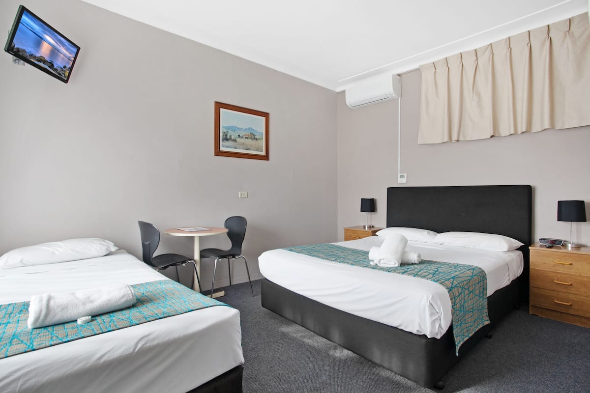 A hotel room with two beds, a desk, a chair, a TV, and a painting on the wall.