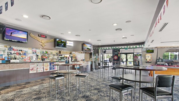 A hotel lobby with a bar area, seating arrangements, and a large screen displaying a sunset scene.
