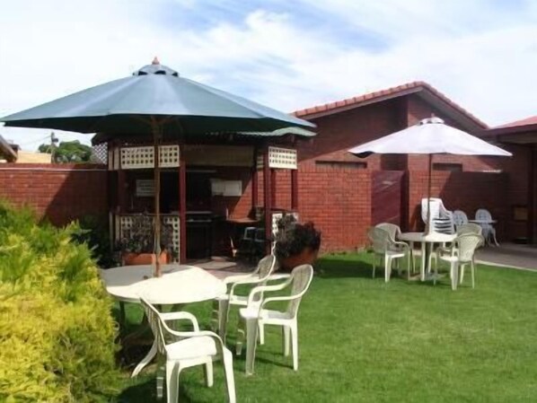 A patio area with outdoor seating, including white plastic chairs and tables, under umbrellas.