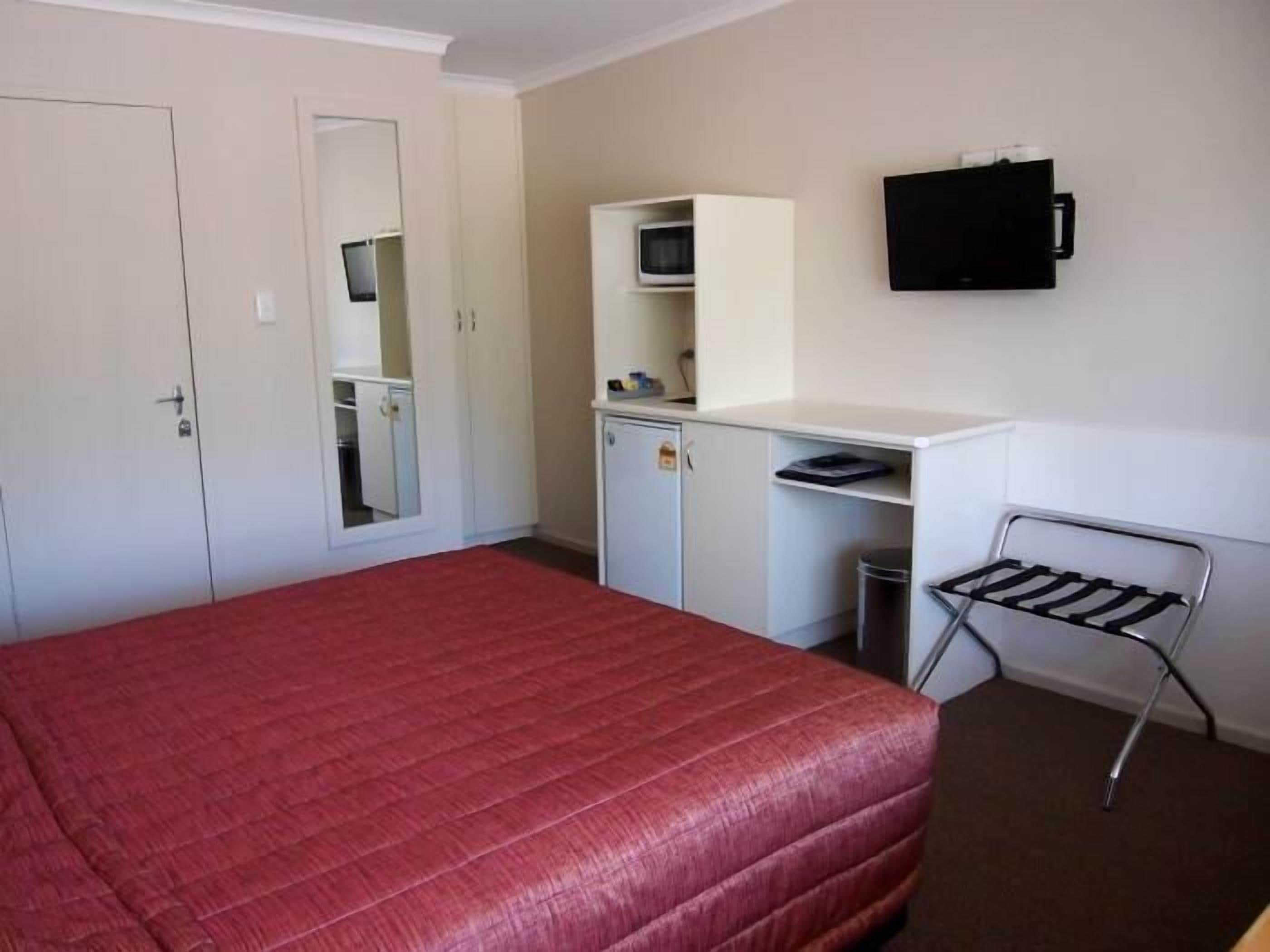 A room with a bed, a desk with a chair, a TV, and a wardrobe.