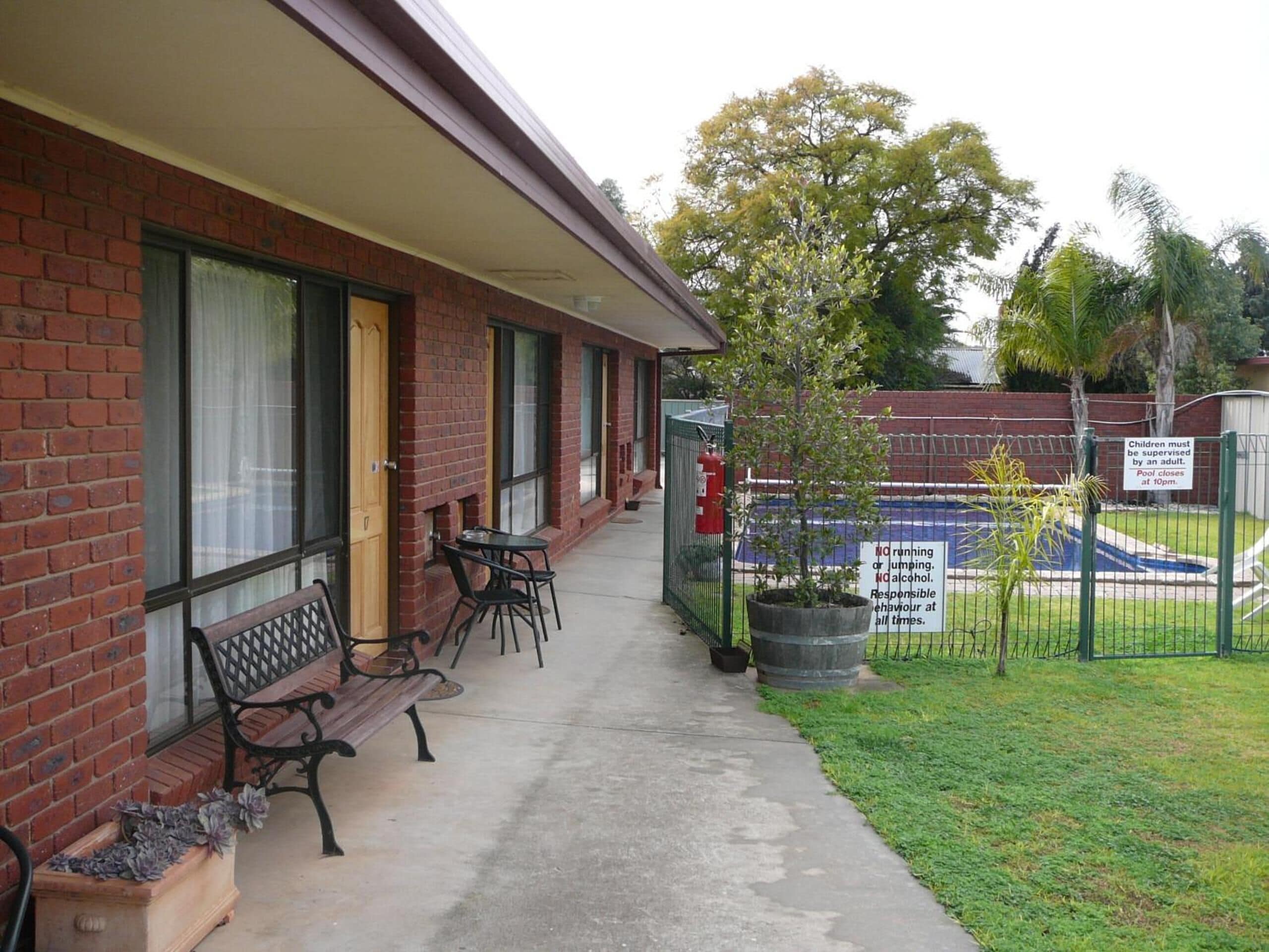 A brick building with a covered patio area, outdoor seating, and a fenced pool area.