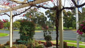 A covered outdoor area with a bench, greenery, and a view of a road and buildings in the background. - Murray River Motel (Swan Hill)