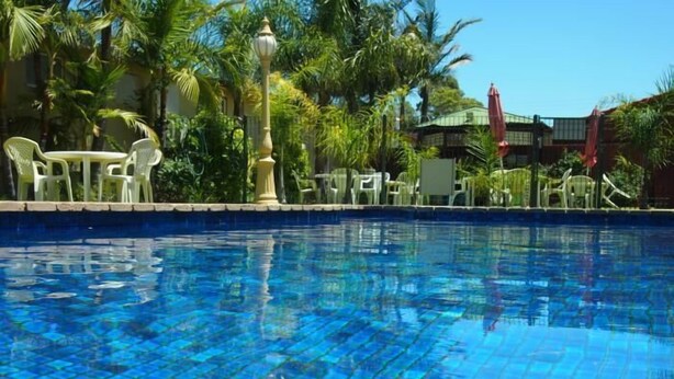 A clear blue pool with tiled edges, surrounded by palm trees and outdoor furniture. - Murray River Motel (Swan Hill)