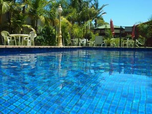 A clear blue pool with tiled edges, surrounded by palm trees and outdoor furniture.
