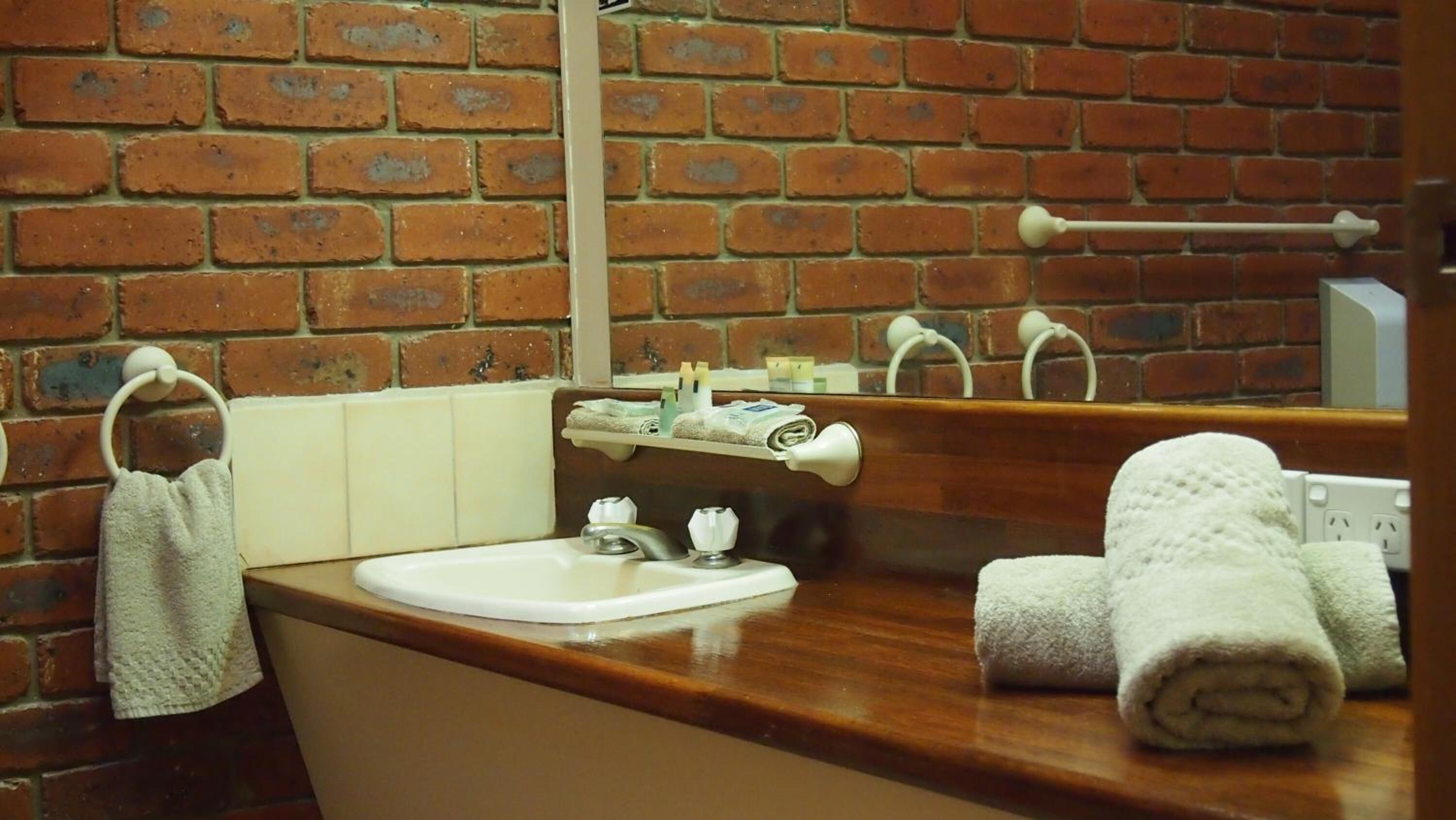 Un baño con pared de ladrillo, lavamanos y espejo.