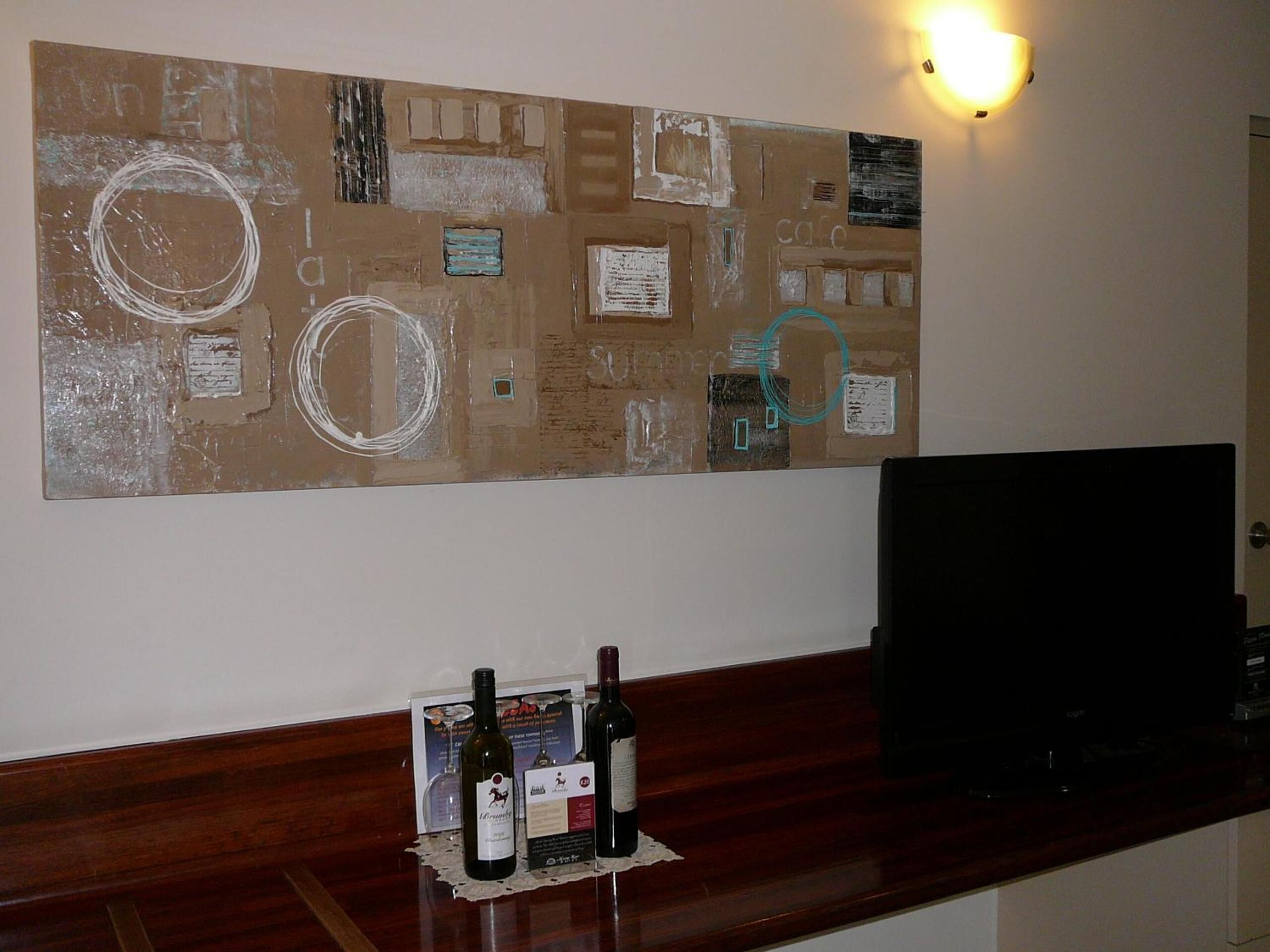 A corkboard with various notes and drawings, a wooden counter with wine bottles, and a television on a stand.