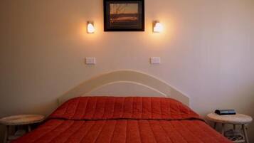 Una habitación con una cama, dos lámparas de pared, un cuadro enmarco y una pequeña mesa con una silla.