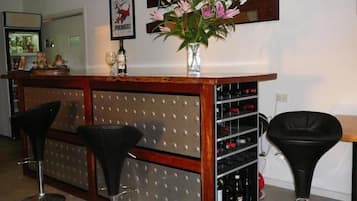 A bar area with a wooden counter, two black bar stools, a wine rack, and a vase with pink flowers.