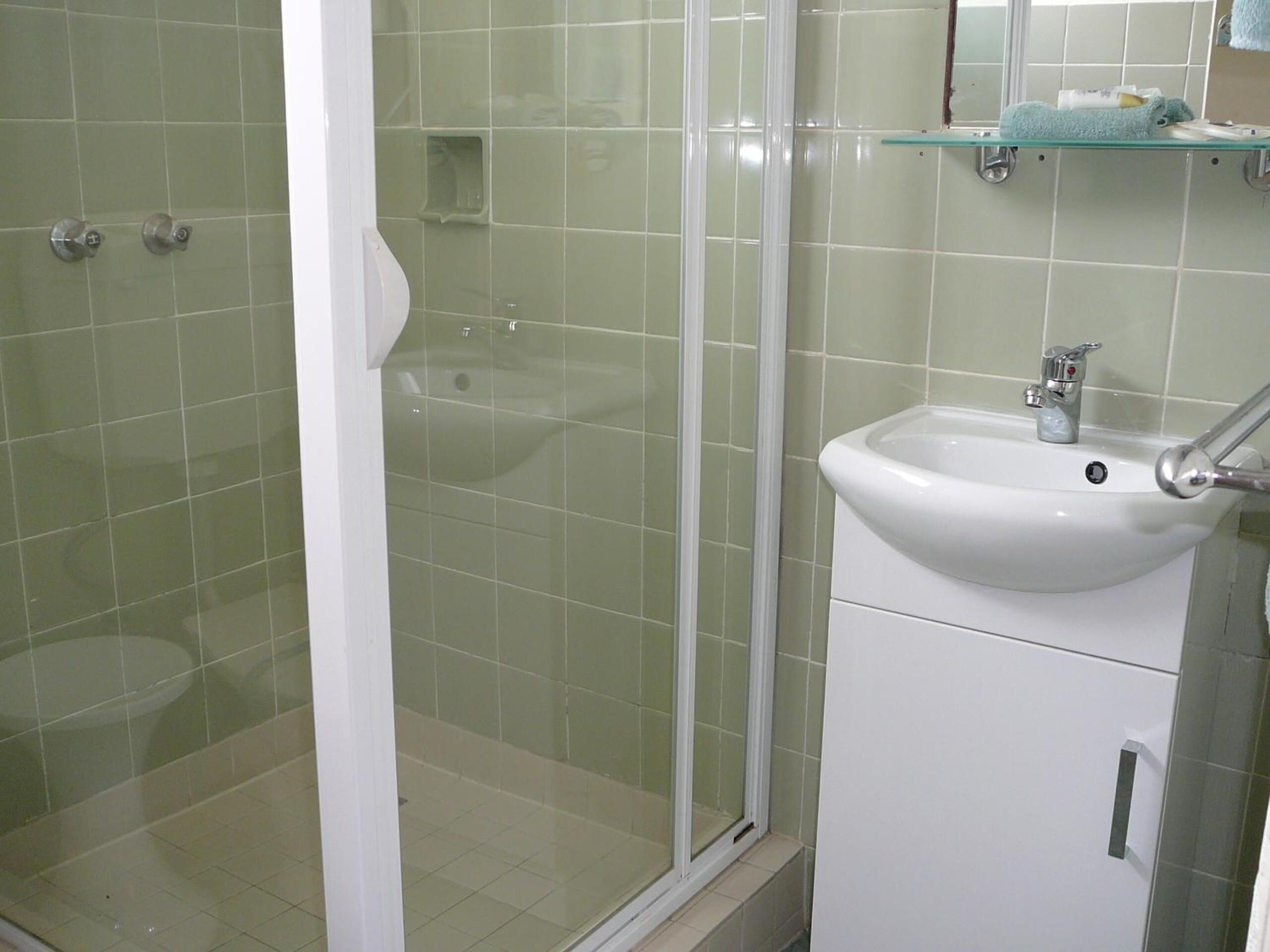 Een badkamer met een douchecabine van glas, een witte wastafel en een glazen plank erboven.