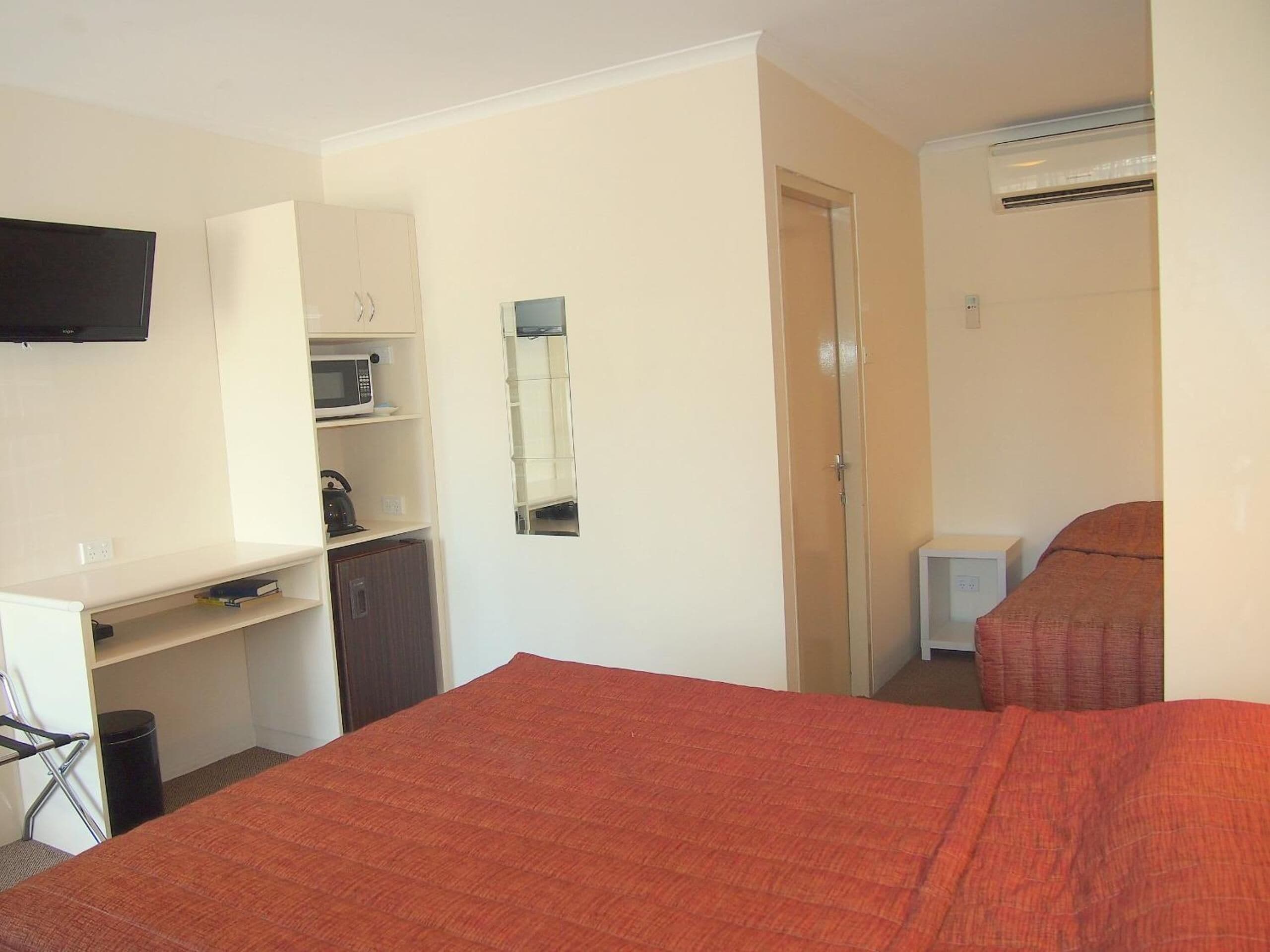 Une chambre à coucher comprenant un lit, une armoire, un bureau avec une chaise, une télévision et une petite table de chevet.
