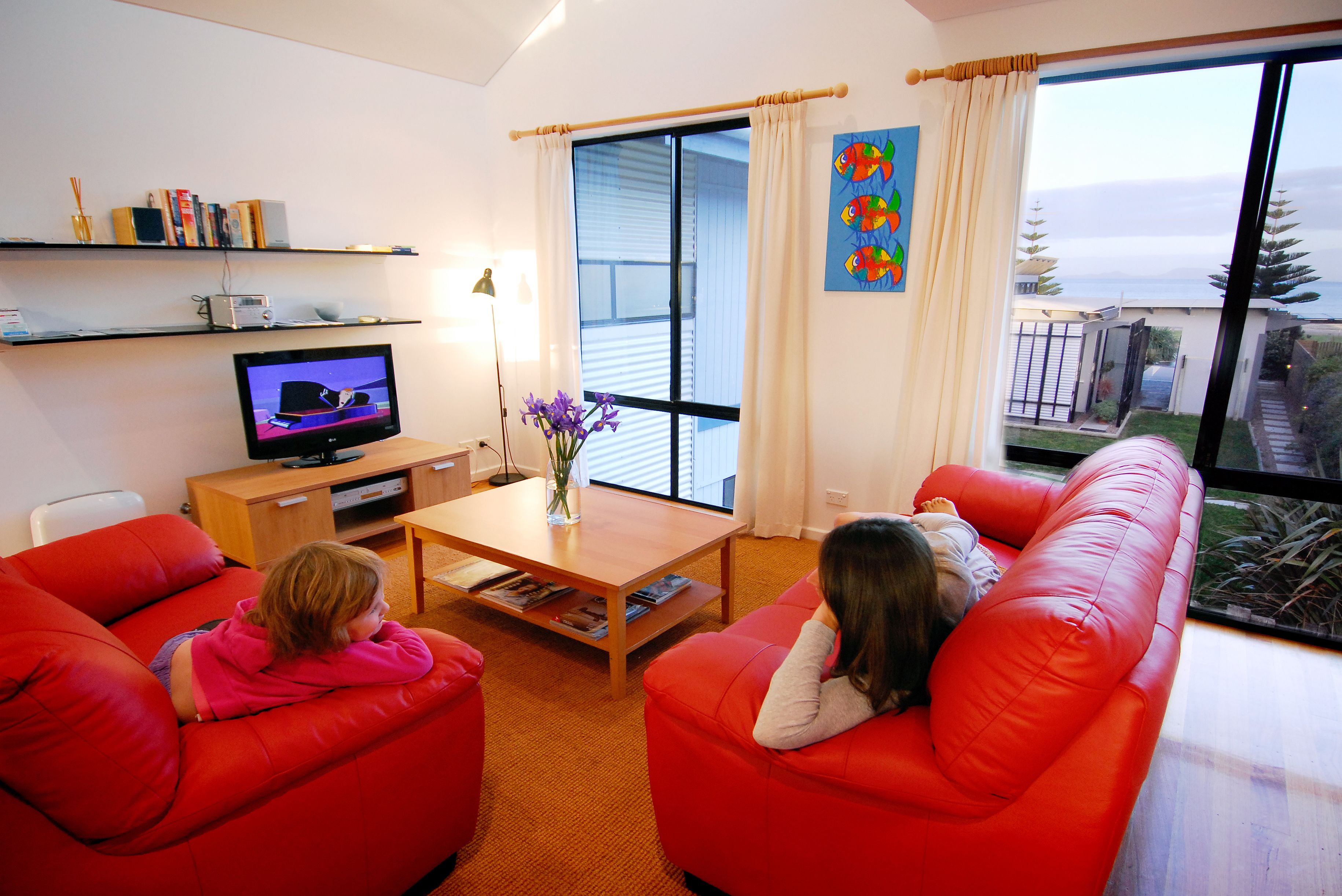 Una sala de estar con dos sofás rojos, un televisor, una mesa de centro y una ventana con vista al mar.