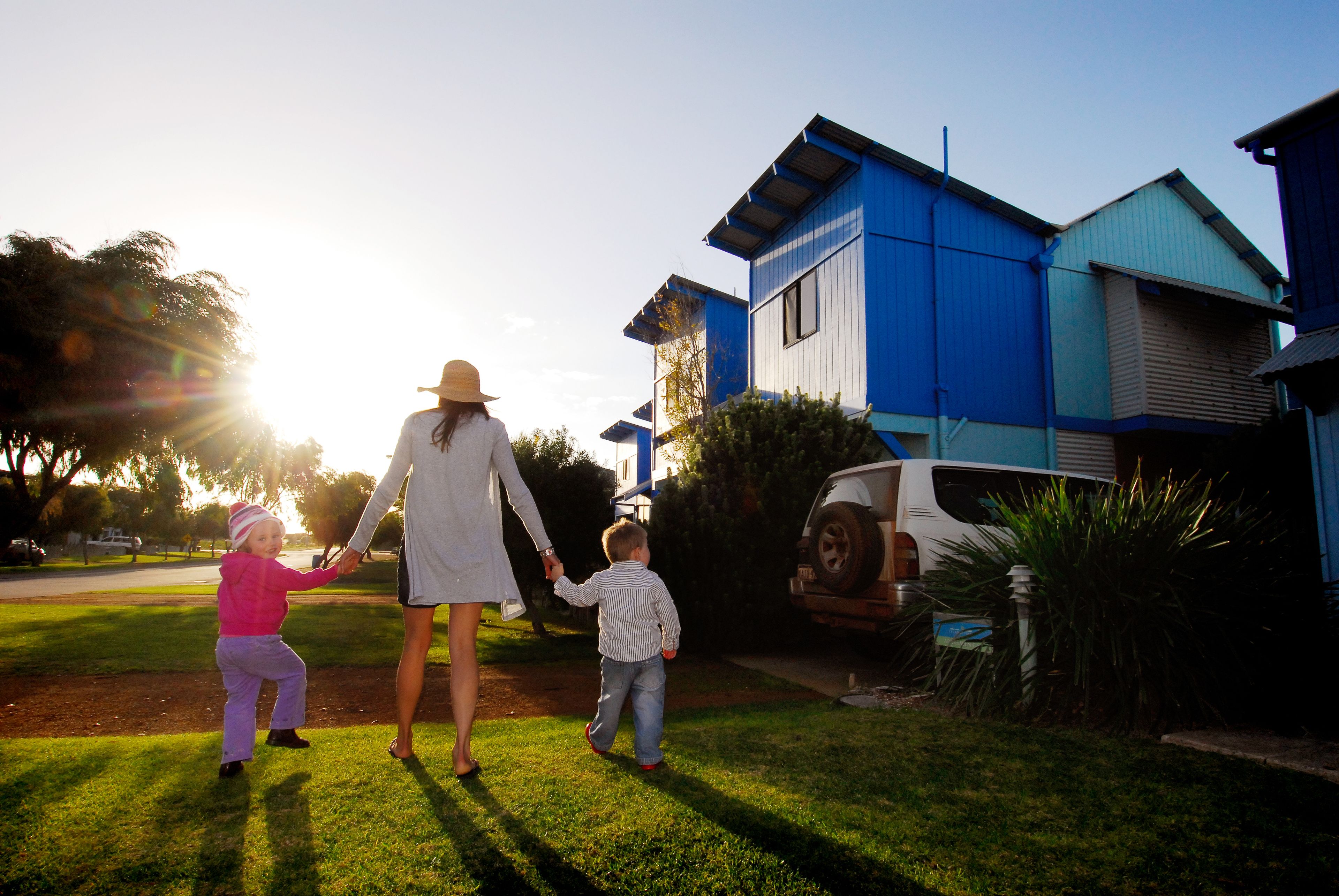 Una famiglia che si tiene per mano su un prato verde, con una casa blu sullo sfondo.