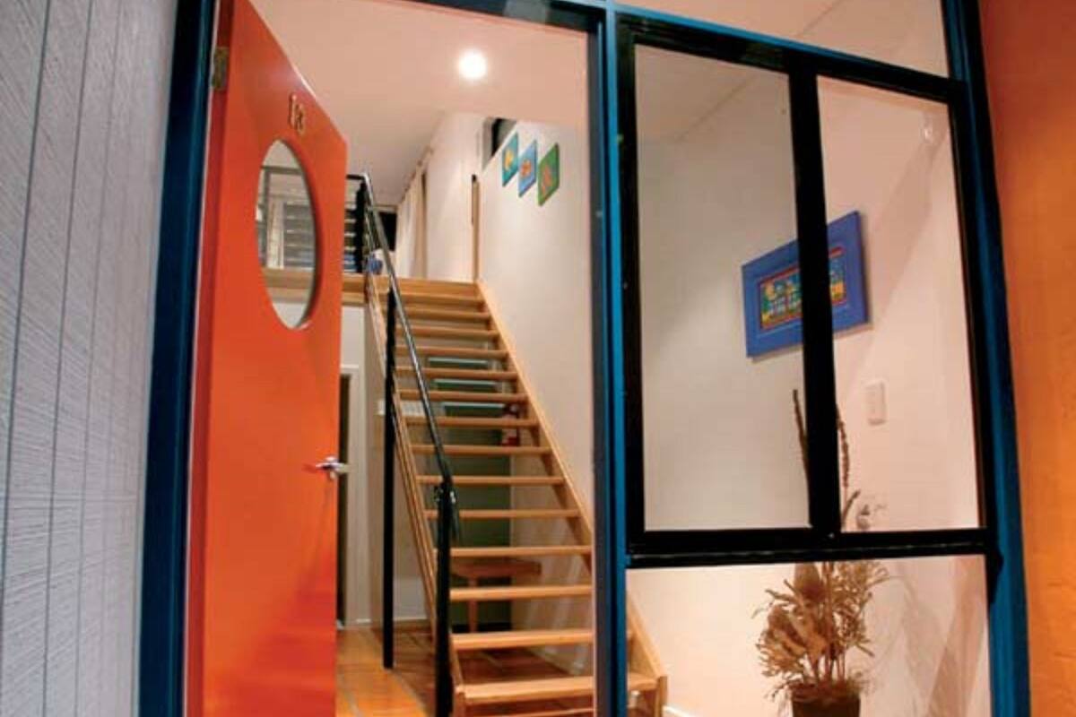 A modern interior with a wooden staircase, a red door, and a large glass sliding door.
