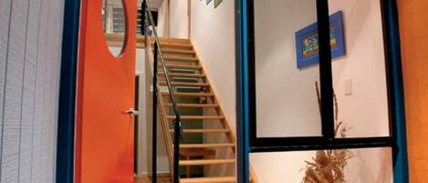 Un interior moderno con una escalera de madera, una puerta roja y un amplio ventanal corredero de vidrio.